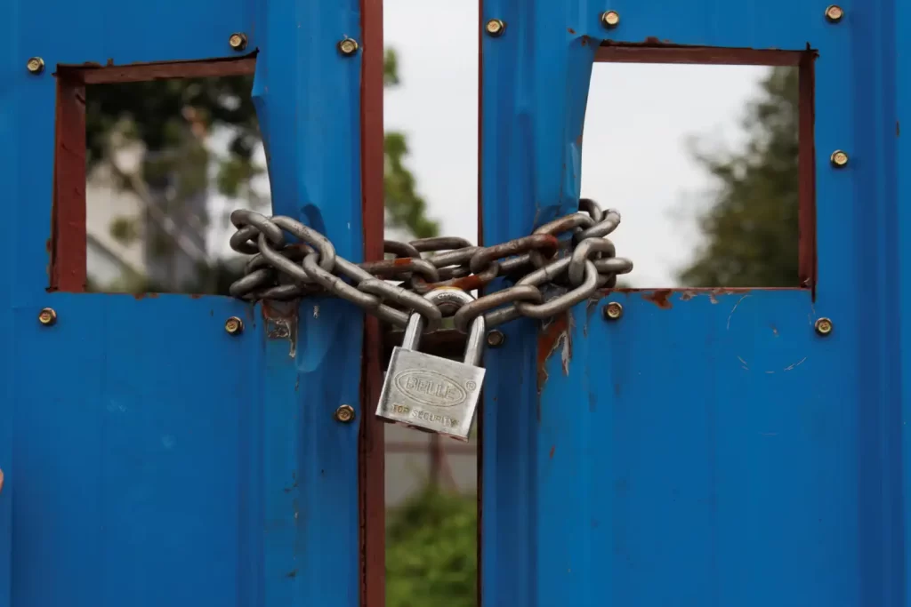 A big silver padlock and chain on a set of blue gates to show that they are closed and locked. This is to show the unlock and lockup services that RSM Property Solutions provides in Oxfordshire, Wiltshire and Gloucestershire.